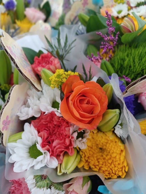 A vibrant floral bouquet featuring an orange rose as the focal point, surrounded by white daisies, pink carnations, yellow chrysanthemums, and purple lavender accents. The flowers are arranged in a co