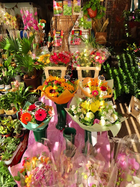 A display of vibrant floral arrangements and bouquets featuring a variety of fresh flowers, including bright pink, yellow, orange, and white blooms, arranged in wrapping paper and vases. The flowers a