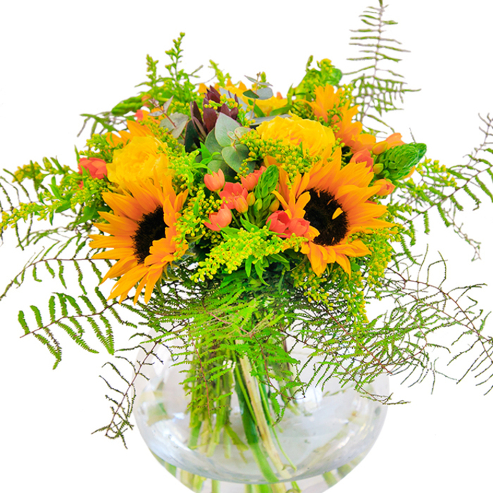 This sun-drenched bouquet channels the best of Noak Hill's seasonal splendor, artfully assembled for those who cherish both nature and warmth. At the heart of the display, majestic sunflowers-each crowned with their dark, textural centers and vibrant yellow petals-radiate like miniature suns, joyfully announcing the season. Nestled amongst them are sumptuous yellow roses, their velvety petals unfurling in classic spirals, adding both fullness and vintage charm to the overall composition. Bright red clusters of Hypericum berries sparkle within the greenery, lending whimsical pops of color that recall the lively market stalls in Noak Hill's nearby communities. A tapestry of green textures-including soft ferns that arc with gentle movement, fine green filler with small yellow blossoms, and elegant vertical flower spikes-forms a backdrop of verdant abundance. Eucalyptus leaves add a silvery hint and soothing scent, reminiscent of the gentle breezes that pass through the area's open woodlands. Everything is gathered within a transparent, globe-shaped glass vase-a modern touch that reveals the bouquet's bold structure and clean lines. Bathed in ambient light, the arrangement becomes the embodiment of happiness and celebration, perfect for birthdays, anniversaries, or moments that call for sincere joy, designed by the skilled hands at Florist Noak Hill. With every glance or breath, this bouquet offers a reminder of the vibrant spirit and fresh beauty that define Noak Hill.