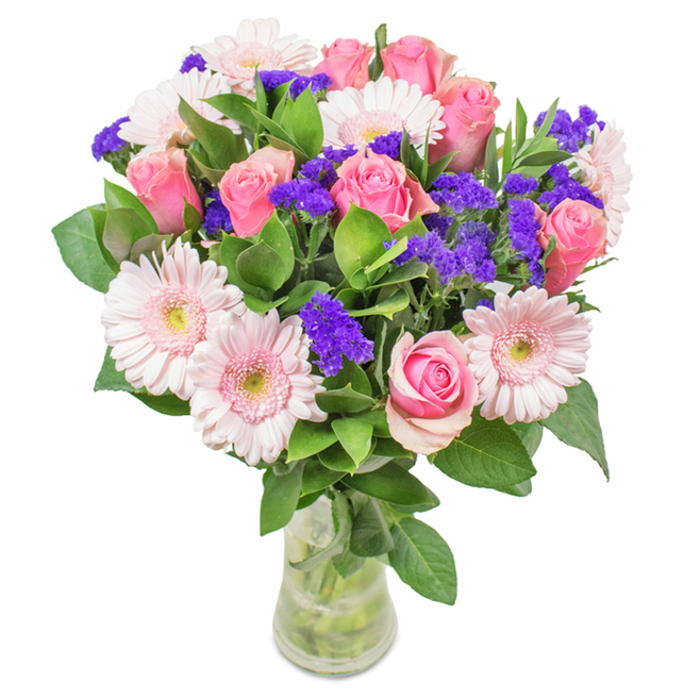 This vibrant floral arrangement, crafted by a florist in Noak Hill, features a harmonious mix of approximately seven to nine soft and medium pink roses, their classic spirals at varying stages-some still teasing with buds, others beginning to blossom with youthful grace. Framing the roses, five to seven blush-pink Gerbera daisies sit with large, round heads and creamy centres, catching attention through their gentle contrast and delicate beauty. Punctuating the bouquet, clusters of vivid purple statice or limonium stand out with bold texture and deeper colour. All are enveloped in a rich bed of deep green foliage, echoing the abundant greenery often admired in Noak Hill's parks and footpaths. Set in a clear glass vase where water and stems are visible, the arrangement radiates freshness and care. This captivating blend, perfect for birthdays, Mother's Day, or as a thoughtful gift for home or office on Noak Hill's leafy streets, conveys heartfelt celebration and the enduring artistry of local floristry.